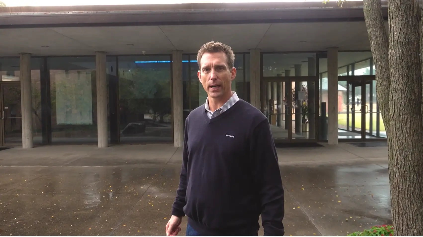 Man in a navy sweater standing outside a building entrance.